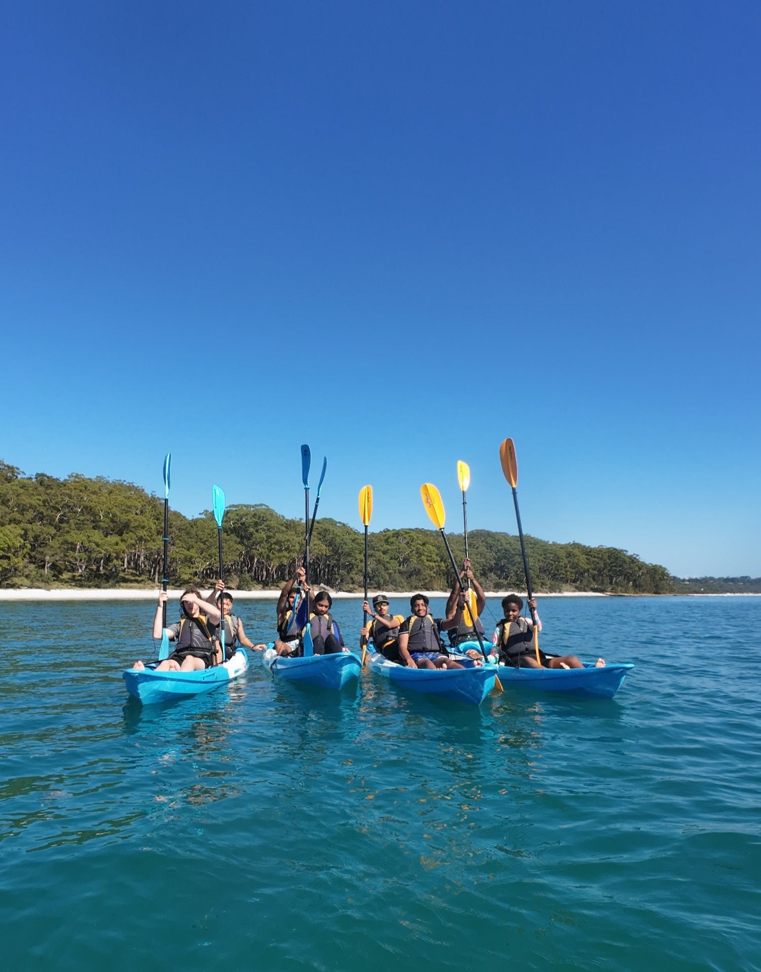 A school group kayaking on a clear blue lake with trees in the background