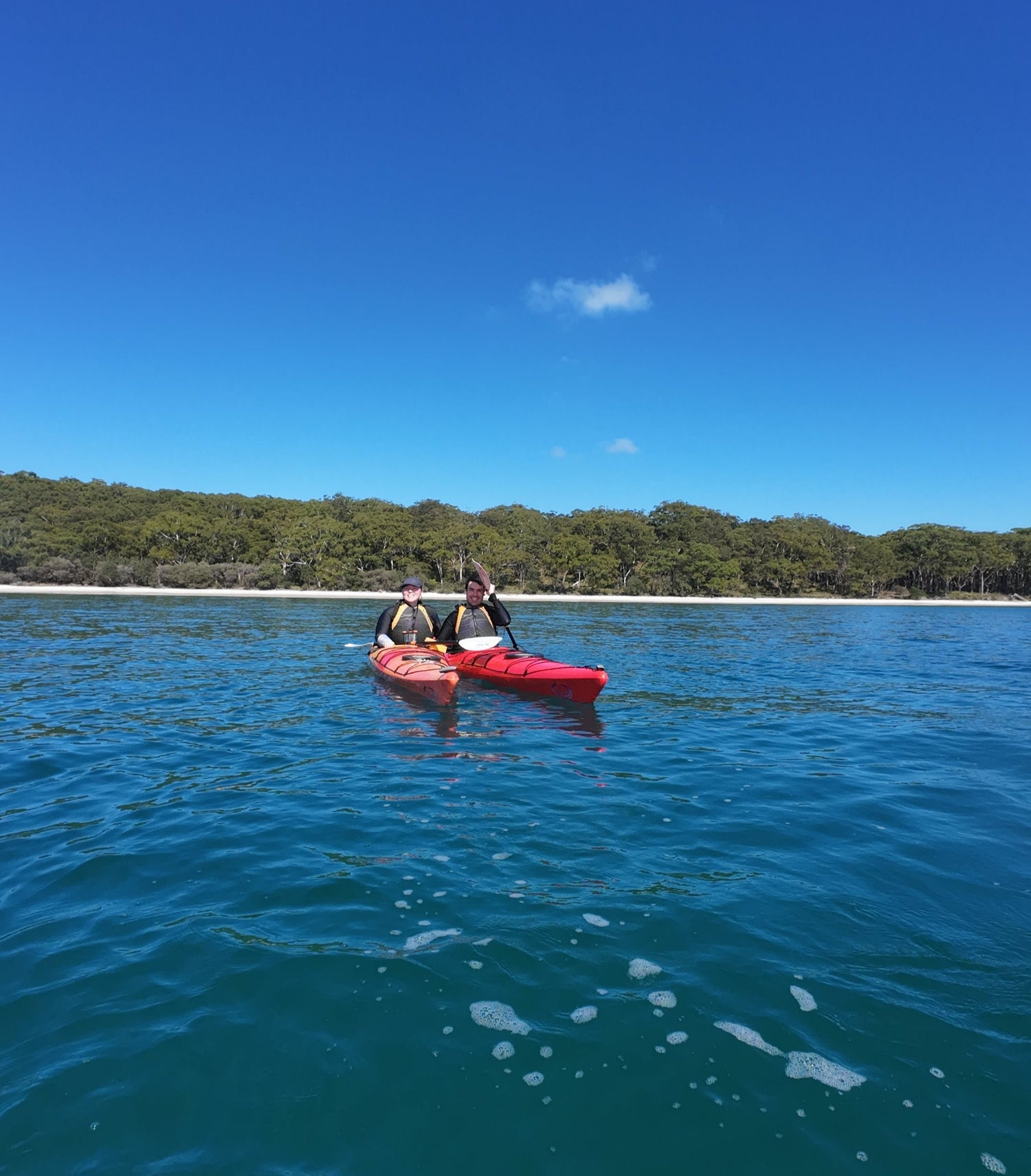 Two people in a kayak on a clear blue body of water with a bright blue sky.