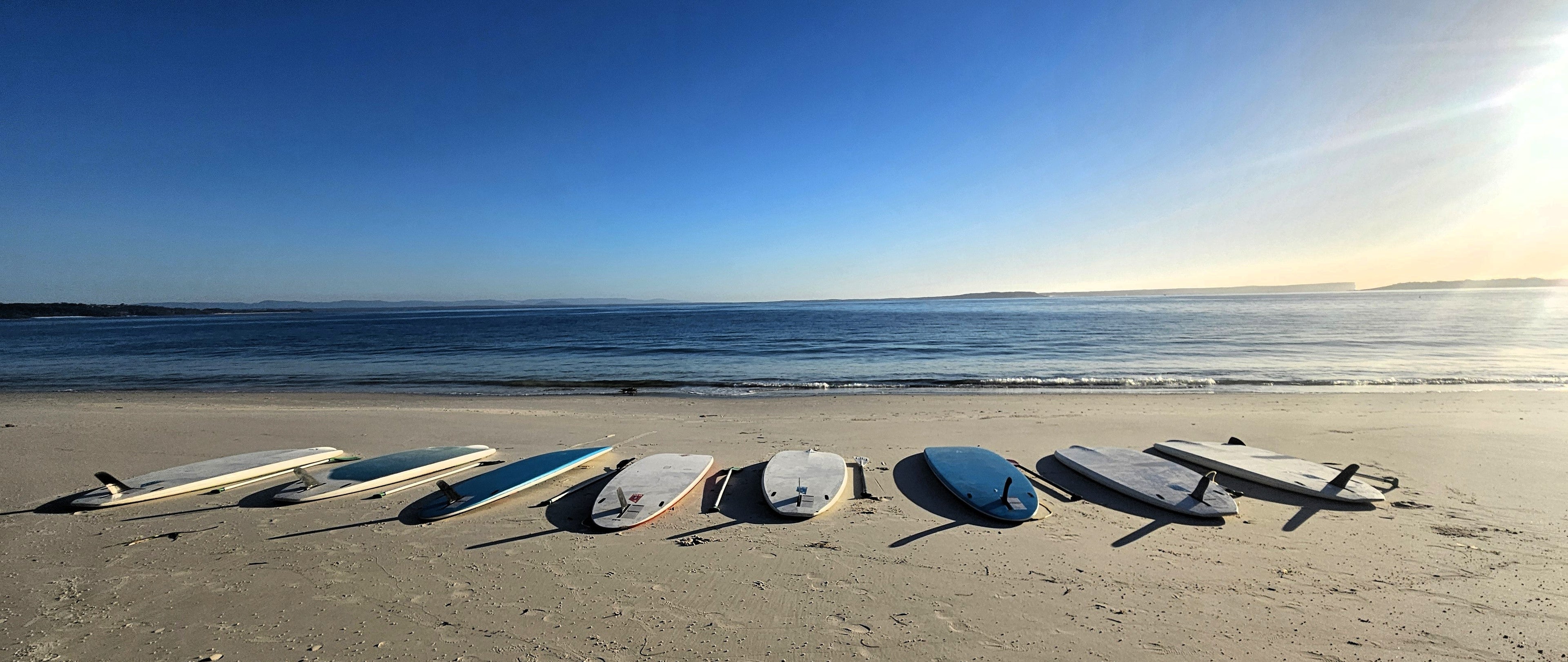 Row of paddleboards on Iluka Beach with a clear blue sky and ocean.