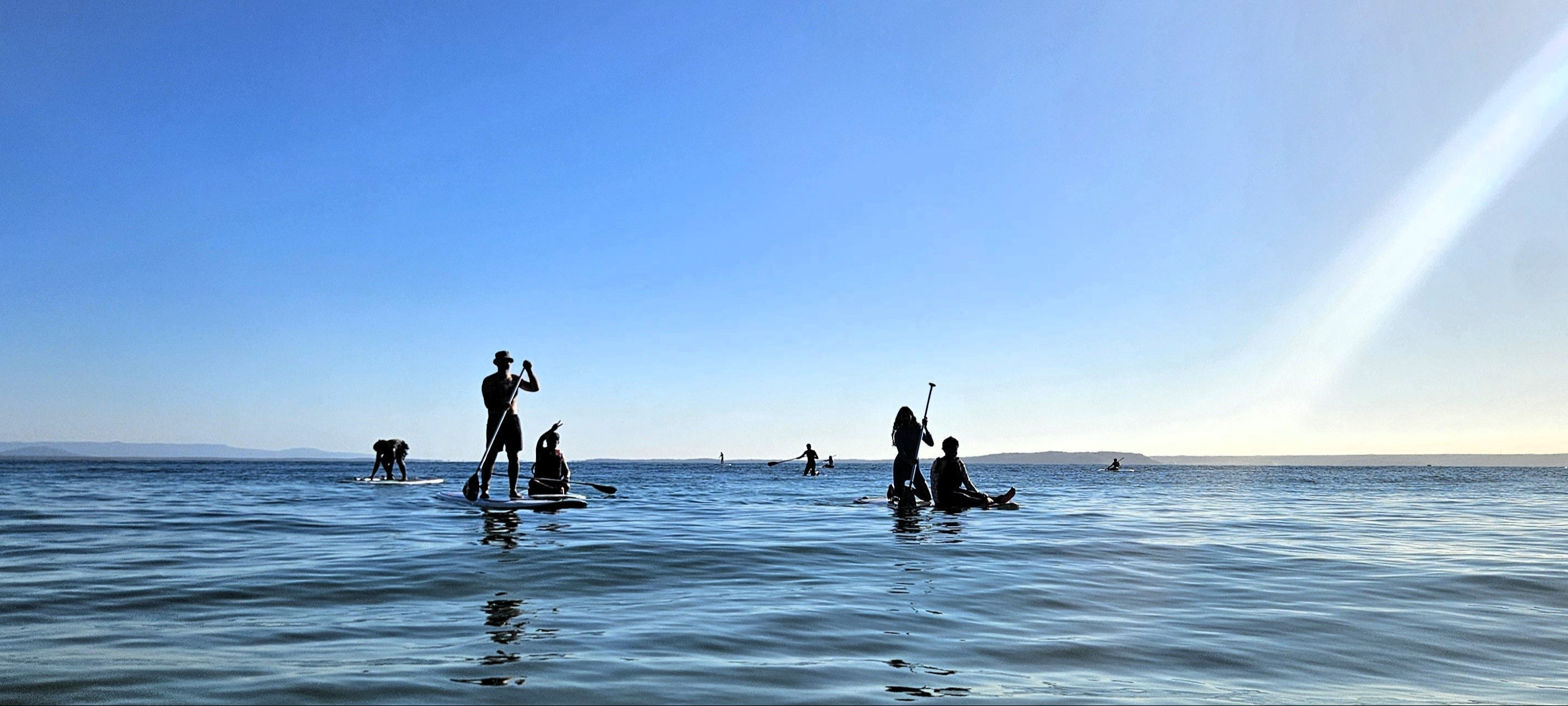 People standing on surfboards in the ocean with a rainbow in the sky.
