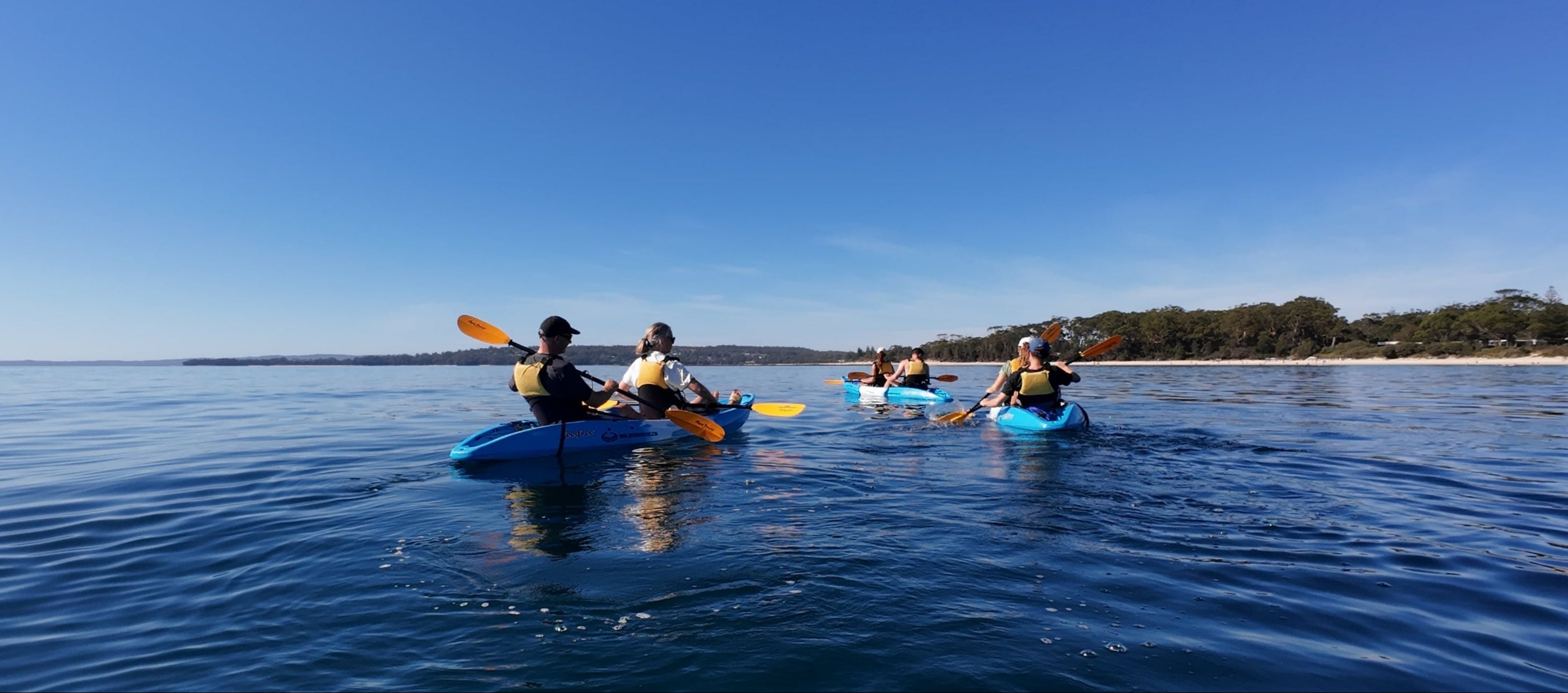 People kayaking on a calm body of water with a clear blue sky.