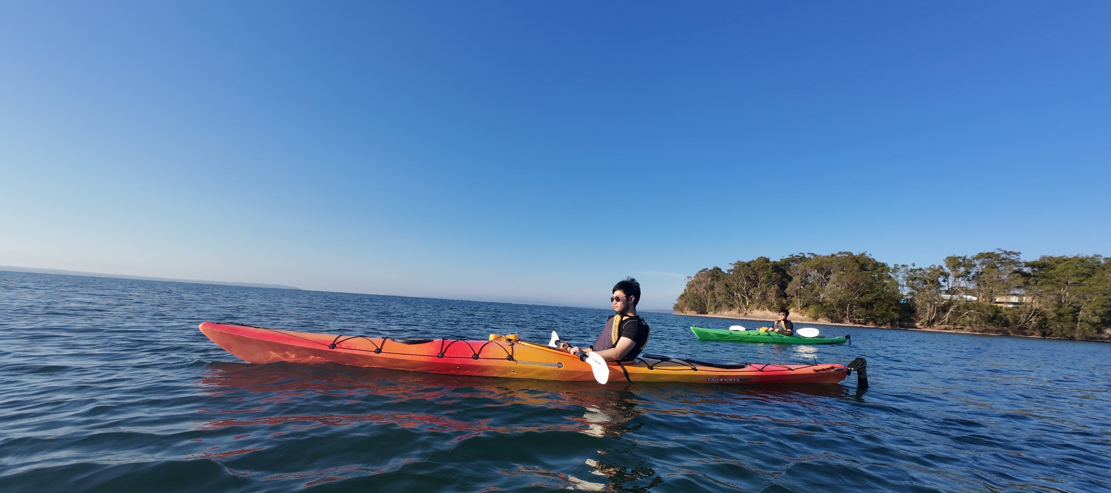 Person kayaking on a calm body of water with clear blue sky