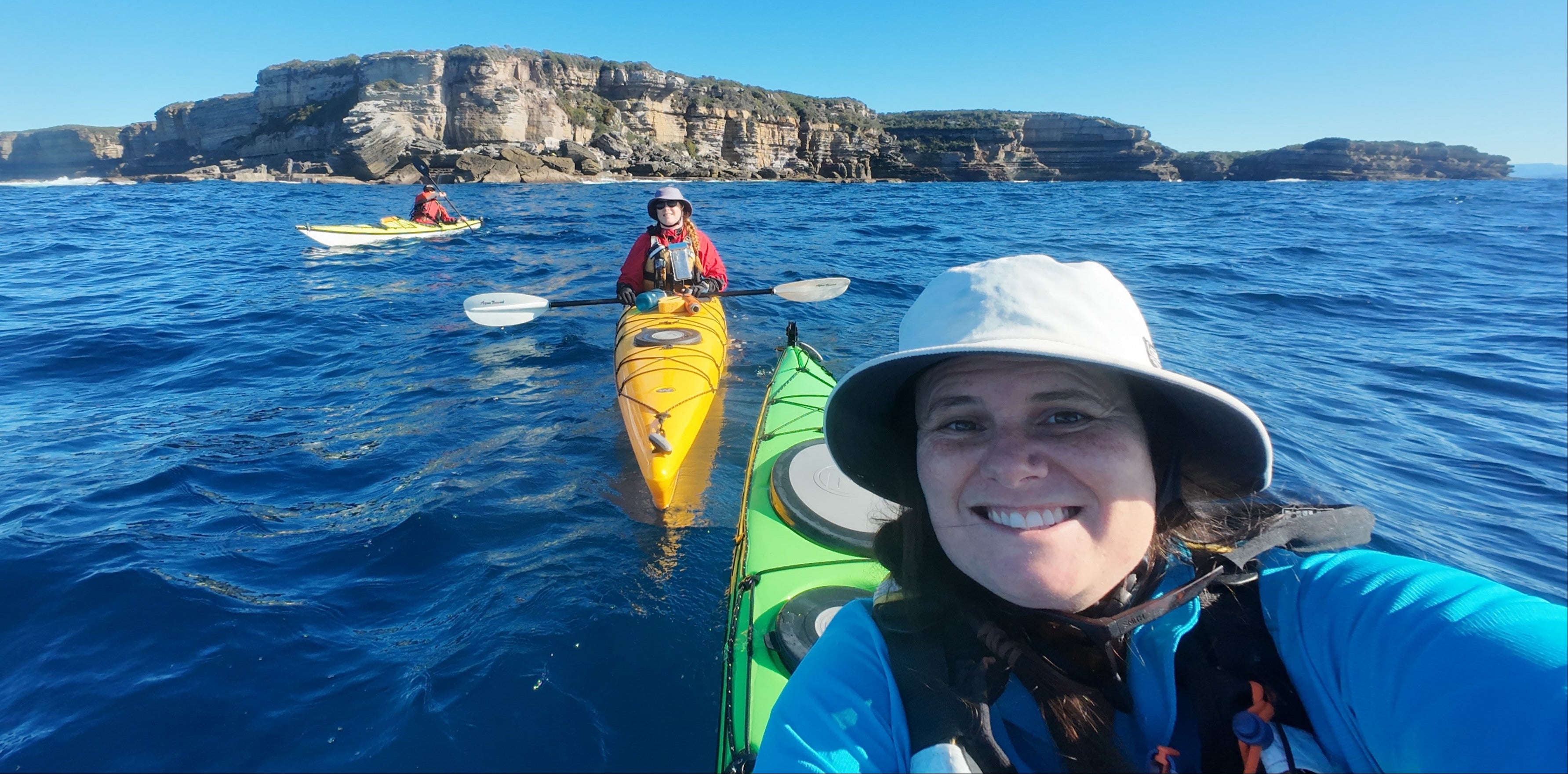Woman kayaking in the ocean with cliffs in the background