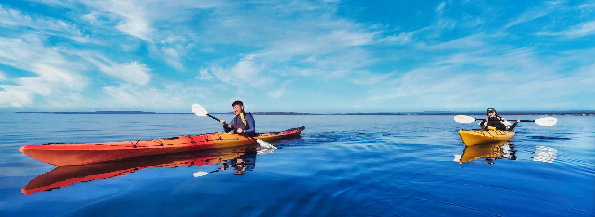 Two kayakers paddling on Jervis Bay with a clear blue sky.